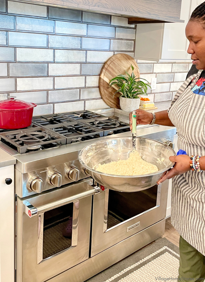 48 inch wide stainless steel commercial style kitchenaid range with two ovens and large gas cooktop. Chef keys with bowl of pancake batter in foreground